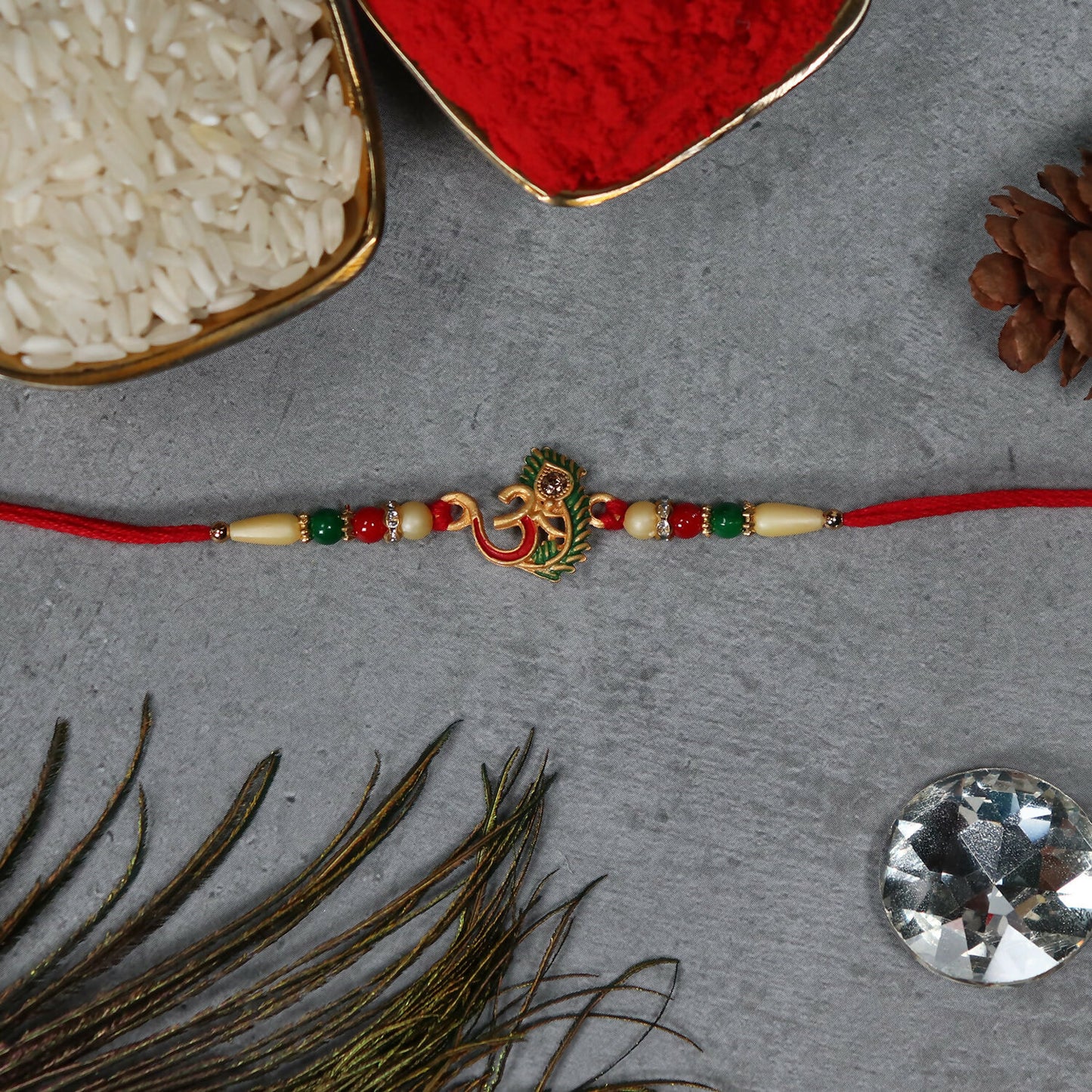Om Peacock Feather Rakhi by Wukusy featuring peacock feathers and intricate designs on a decorative thread.