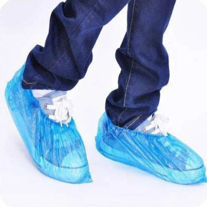 Set of 100 disposable plastic shoe covers with elastic fit by Wukusy, shown in a natural, practical arrangement.