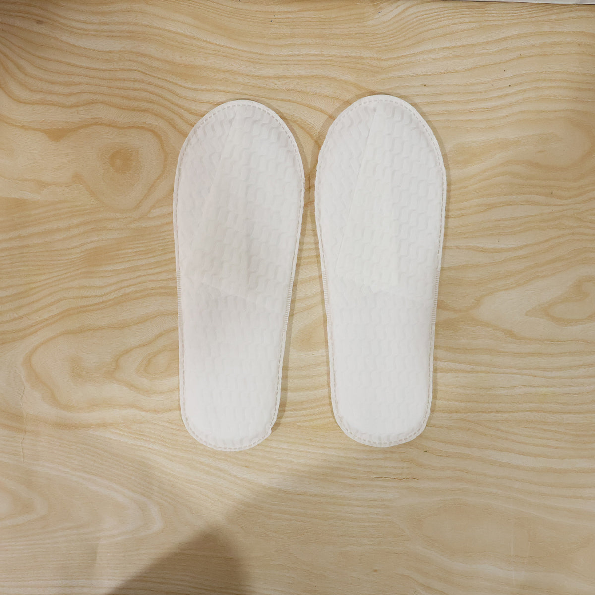 Pair of white disposable hotel slippers by Wukusy for guest comfort, shown in a close-up image.