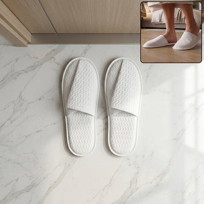 Pair of white disposable hotel slippers for guests by Wukusy, shown in a clean, open-toe design on a hotel room floor.