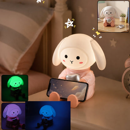 Wukusy rabbit LED night light with mobile phone stand on bedroom or study table, soft lighting and convenient phone holder.